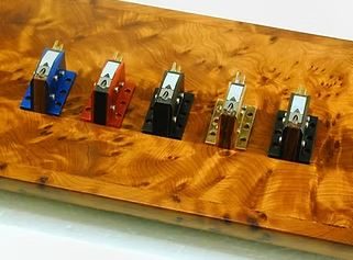 Audio Note (UK) Moving Coil Tonabnehmerserie (blau, rot, schwarz, gold & schwarz) von oben auf eine Holzuntergrund aufgenommen.