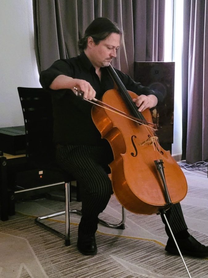 Ein Mann spielt in Duett mit einer Audio Note High-end HiFi-Anlage Cello in einem modernen Raum mit Vorhängen.