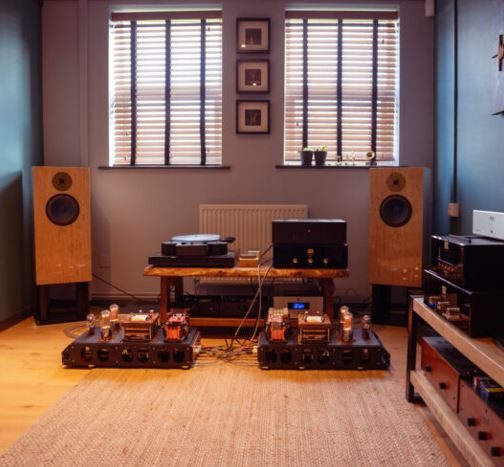 High-end Musikanlage mit Lautsprechern, Verstärkern und Holzmöbeln in einem gemütlichen Raum.