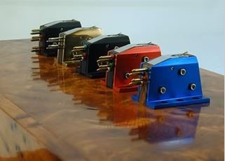 Fünf Audio Note (UK) Moving Coil Tonabnehmer (blau, rot, schwarz, gold & schwarz) aufgereiht auf eine hochglanz polierte Holzuntergrund.